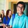 Happy Indian high school student using phone outside classroom